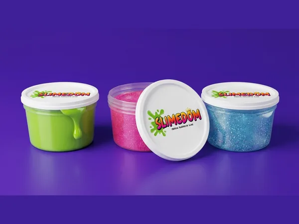 Three Slimedom tubs of green, pink and blue slime on a flat purple ground, one lid propped against the middle tub.