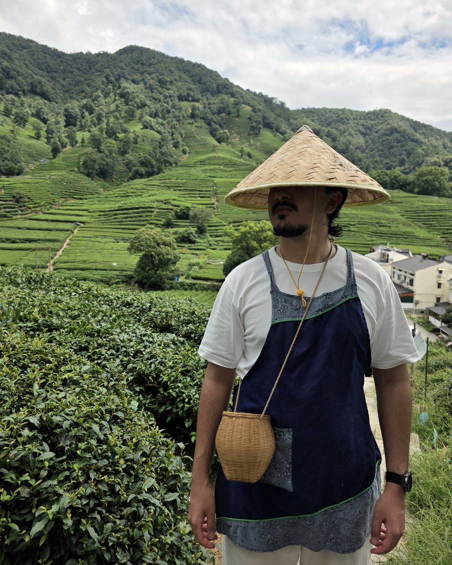 Salman in a conical straw hat, standing in front of terraced tea fields.