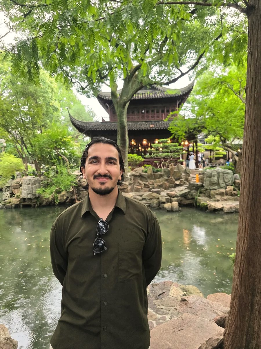 Salman in a classical Chinese garden, a wooden pavilion and a pond behind him.